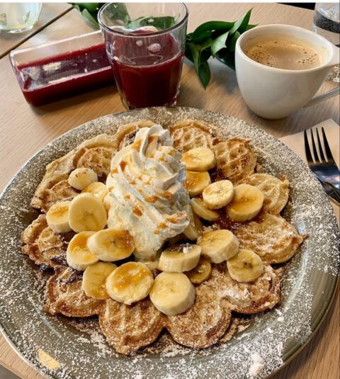 Våffla med banan och grädde till frukost, med kaffe och juice bredvid